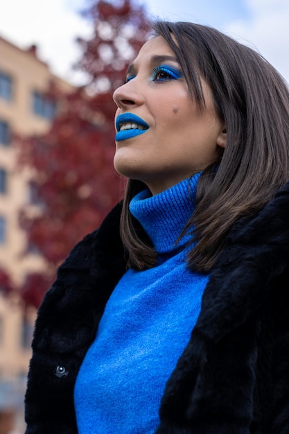 portrait of a smiling young woman with blue eye make-up and lipstick and blue sweater on a nature background.