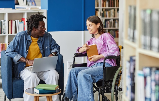 Portrait of smiling young woman with disability talking to friend while studying together in library