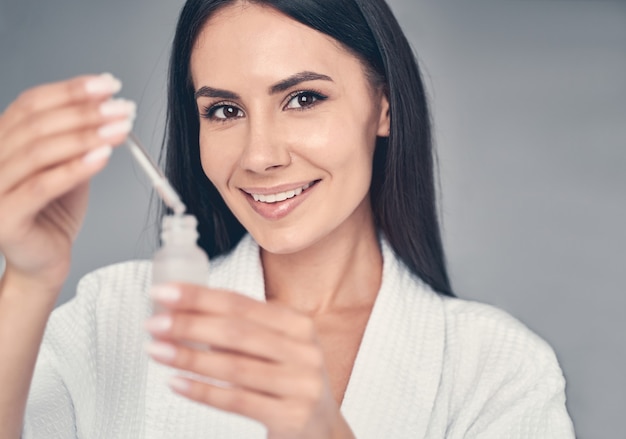 Portrait of a smiling young woman with a face serum looking in front of her