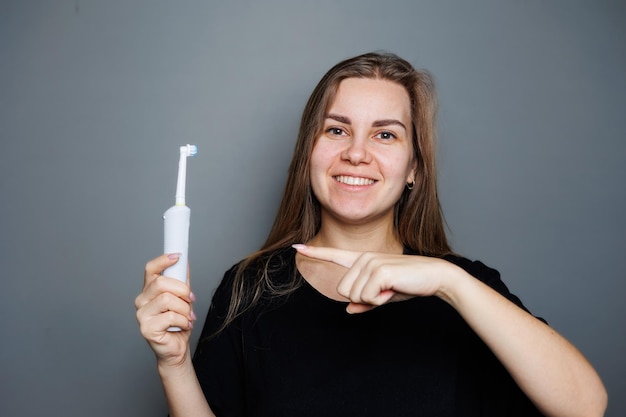 Portrait of a smiling young woman without makeup in a black tshirt brushing her teeth mature woman natural beauty concept Morning brush for teeth dental ultrasonic brush