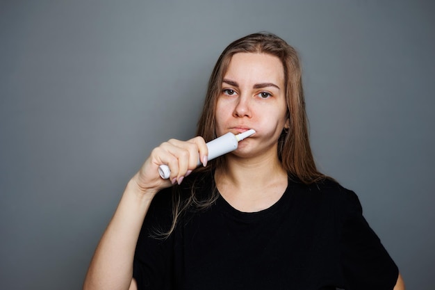 Portrait of a smiling young woman without makeup in a black tshirt brushing her teeth mature woman natural beauty concept Morning brush for teeth dental ultrasonic brush