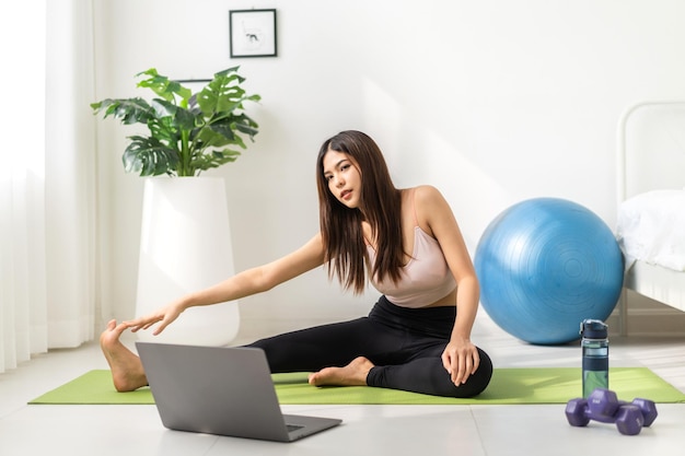 Portrait sport asian beauty body slim woman in sportswear sitting relax and girl practicing yoga and do fitness exercise with laptop computer in bedroom at homeDiet conceptFitness and healthy