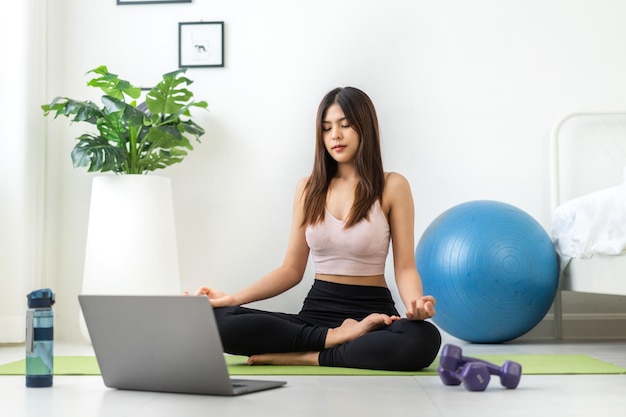 Portrait sport asian beauty body slim woman in sportswear sitting relax and girl practicing yoga and do fitness exercise with laptop computer in bedroom at homeDiet conceptFitness and healthy