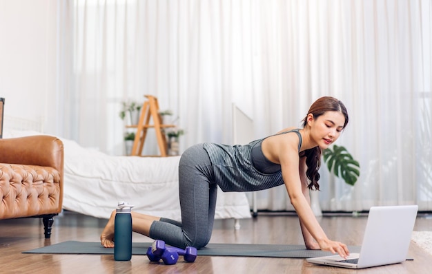 Portrait sport asian beauty body slim woman in sportswear sitting relax and girl practicing yoga and do fitness exercise with laptop computer in bedroom at homeDiet conceptFitness and healthy