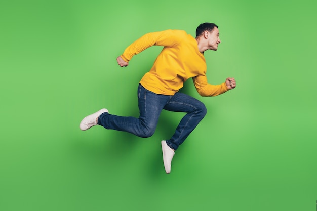 Portrait of sporty energetic guy jump run look empty space on green background