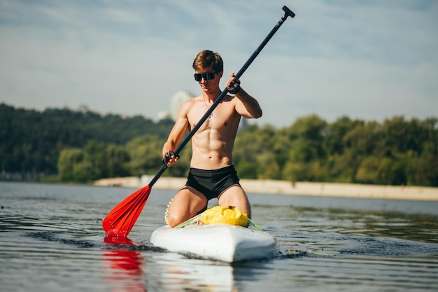 Portrait of a sporty young man rowing on the water on a sup board