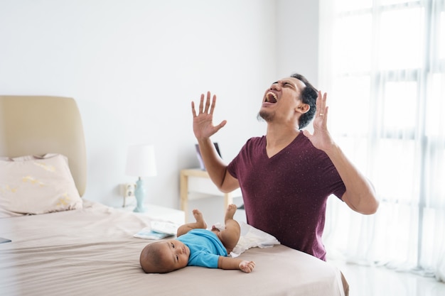 Portrait of stressed asian father changing his infant baby diaper at home