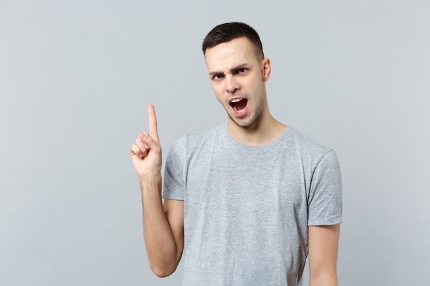 Portrait of strict irritated young man in casual clothes swearing, pointing index finger up 