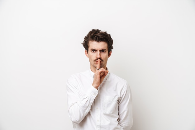 Portrait of strict mustached man wearing shirt holding finger at his lips isolated on white