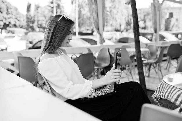 Portrait of a strong independent successful businesswoman wearing smart casual clothing and glasses working on a laptop in a cafe Black and white photo