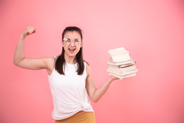 Portrait of a student girl with glasses on a pink wall posing with books in her hands. Concept of education and Hobbies.