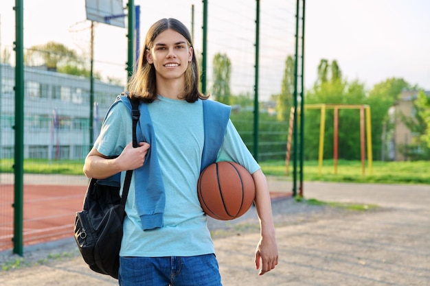 Portrait of student guy with backpack ball near outdoor basketball playground