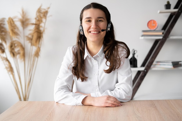 Portrait of student posing at home work desk in headset Teenage female looking at camera distracted of learning using modern techGirl operator in headphones smiling while talking with a client