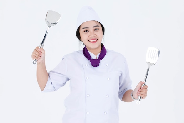 Portrait studio shot of Asian professional restaurant cooking female executive chef in cook uniform standing smiling look at camera holding spatula flipper turner on white background.