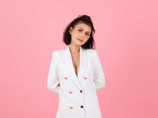 Portrait studio shot of Asian sexy curly hairstyle professional successful businesswoman in white fashionable casual suit with lace lingerie crop top bra standing look at camera on pink background