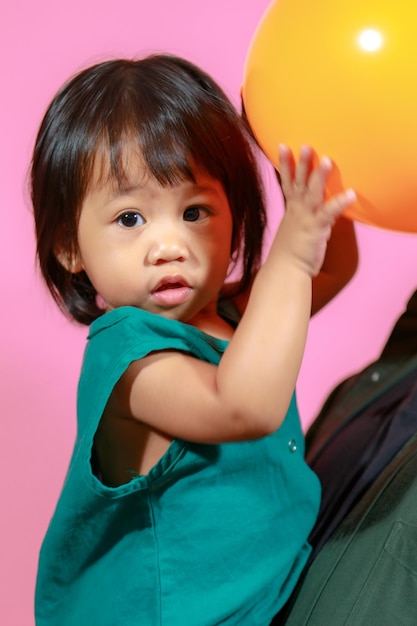 Portrait studio shot little cute Asian kindergarten preschooler girl daughter model in casual long dress holding colorful balloons on pink background