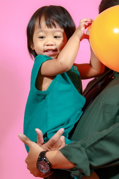 Portrait studio shot little cute Asian kindergarten preschooler girl daughter model in casual long dress holding colorful balloons on pink background