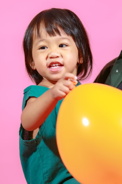 Portrait studio shot little cute Asian kindergarten preschooler girl daughter model in casual long dress holding colorful balloons on pink background