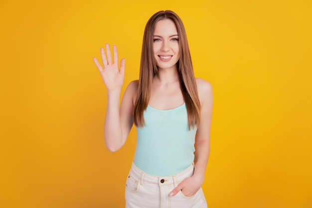 Portrait of stunning lovely lady hand pocket wave palm toothy beaming smile on yellow background