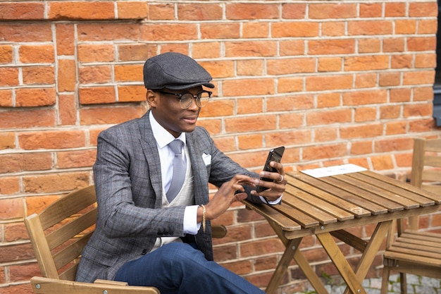 portrait of stylish african man with phone on brick wall background