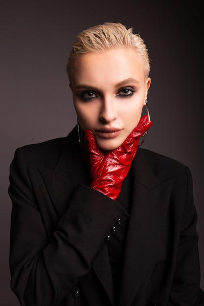 Portrait of a stylish blonde with red leather gloves on a gray isolated background. Earrings in the form of large rings.