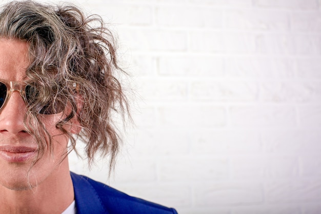 Portrait of stylish businessman with curly long hair in sunglasses smiling at the camera on white background