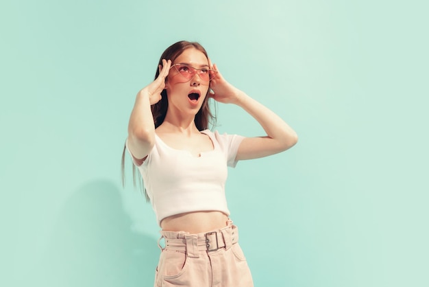 Portrait of stylish emotive young girl posing in pink sunglasses isolated over mint background Shocked expression