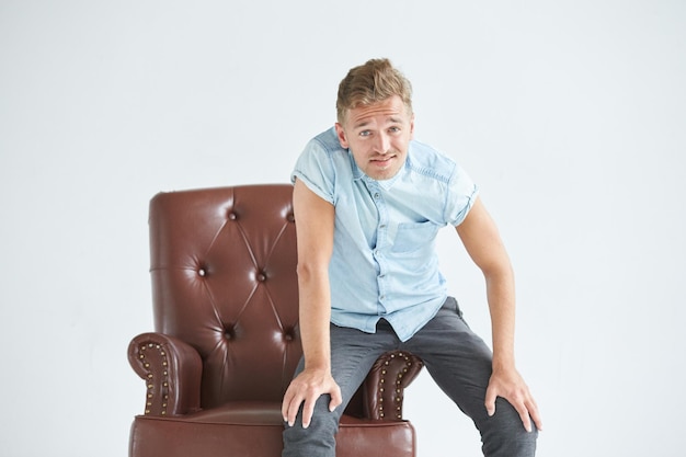 Portrait of a stylish intelligent man small unshaven charismatic blue shirt sitting on a brown leath