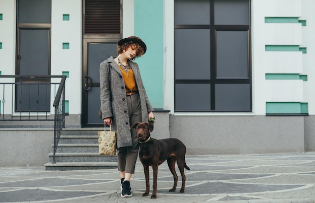 portrait of a stylish lady in a coat and hat on a walk with a pet on the street of the town