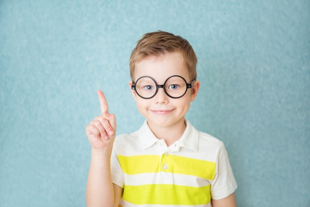 Portrait of stylish little boy with finger pointed up. Kid on blue blackboard. Success, bright idea, creative ideas and innovation technology concept