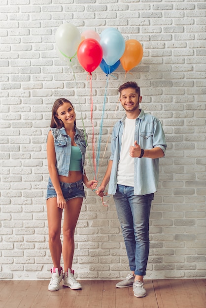 Portrait of stylish teenage couple holding balloons.