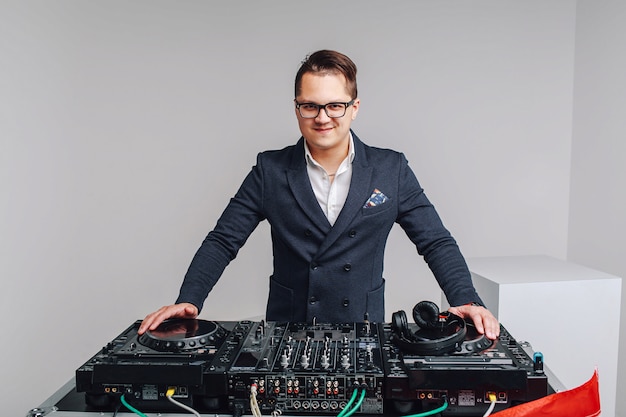 Portrait of stylish young man in formal suit and glasses standing at Dj mixer on light studio background