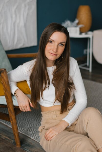 Portrait of a stylish young woman sitting on the floor near an armchair