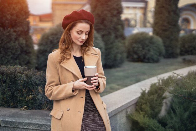 Portrait of stylish young woman wearing autumn coat and red beret outdoors. Pensive beautiful young