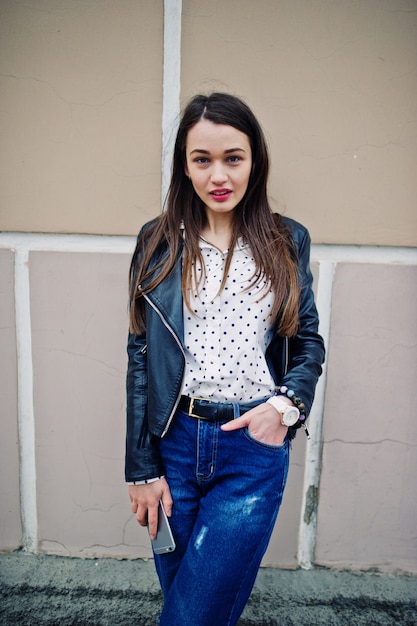 Portrait of stylish young woman wearing on leather jacket with mobile phone at hand