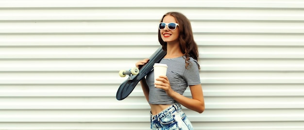 Photo portrait of stylish young woman with skateboard and cup coffee on white background