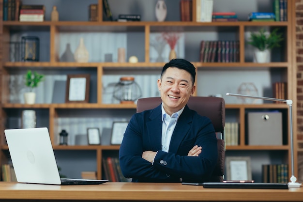 Portrait of a successful Asian businessman in a classic office working on a laptop smiling