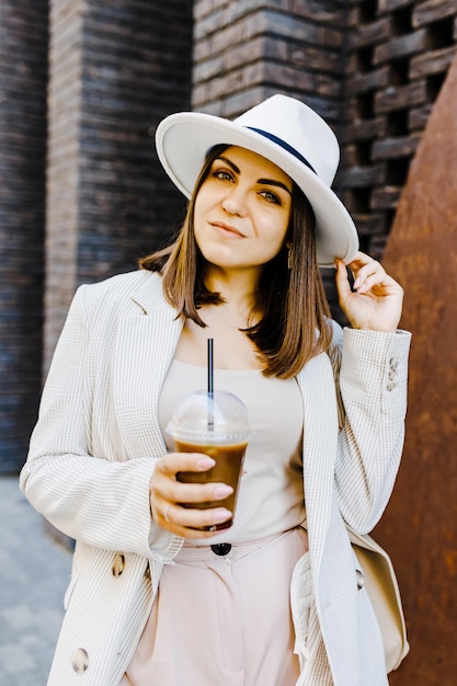 Portrait of successful business woman holding cup of cold drink in hand on her way to work on city street