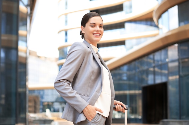 Portrait of successful business woman traveling with case at airport. Beautiful stylish female travel with luggage.