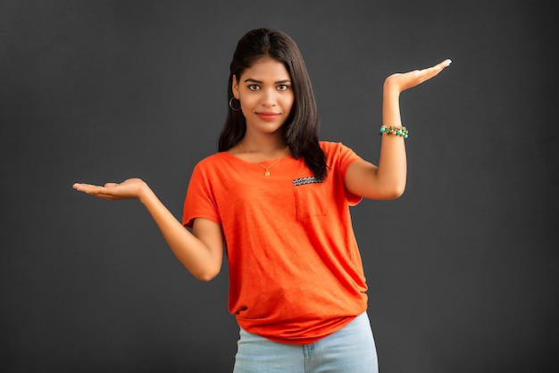 Portrait of a successful cheerful young girl holding and presenting something on hand with a happy smiling face