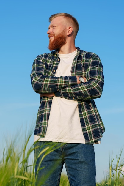 Portrait of a successful farmer A man stands in a wheat field in a shirt and jeans Blue sky on the background