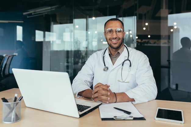 Portrait of successful male doctor hispanic smiling and looking at camera doctor in medical gown