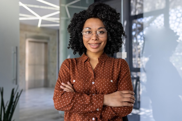 Portrait of successful office worker african american woman with curly hair smiling and looking at