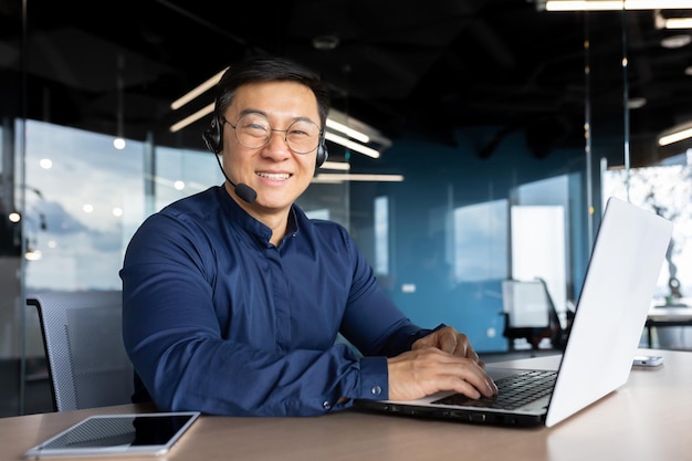 Portrait of successful office worker with headset for video call asian man smiling and looking at