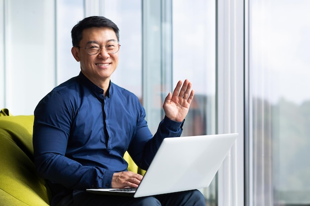 Portrait of successful smiling asian man inside office man smiling and looking at camera near window