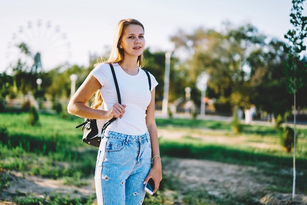 Portrait of successful smiling young hipster girl 20s walking and enjoying summer weather