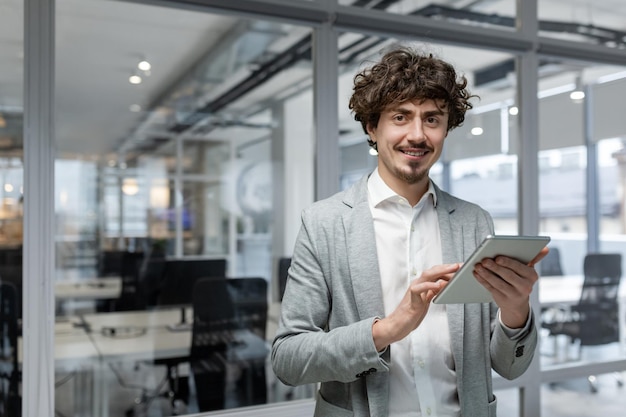 Portrait of successful young businessman man with tablet computer in hands smiling and looking at