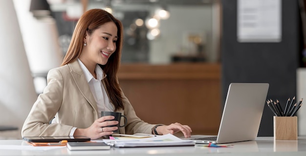 Portrait of Successful Young Businesswoman Sitting at Her Desk Working on Laptop Computer