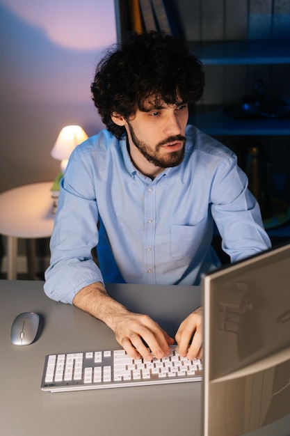 Portrait of successful young man typing online message sitting at table and looking at camera