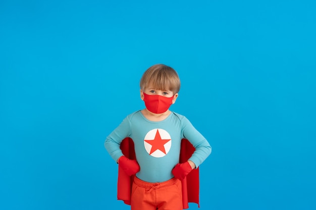 Portrait of super hero kid against blue paper wall.